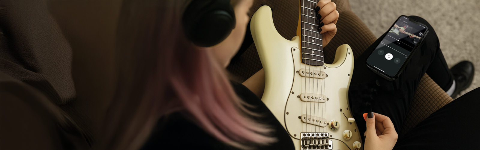 Electric guitar player with headphones using an app on a mobile device to adjust headphone amp controls.